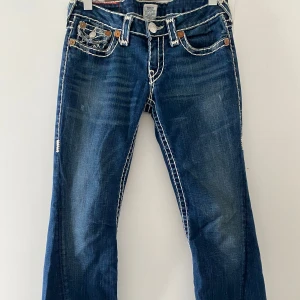 True Religion jeans - Lågmidjade utsvänga jeans från True Religion med snygga detaljer.  Är i storlek 29. Innerbenslängd ca 75 cm Midja: 36cm tvärsöver