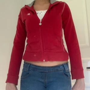 Röd hoodie från Nike - Säljer en snygg röd hoodie från Nike med dragkedja och huva. Den har en stor vit Nike-logga på ryggen och en mindre logga på bröstet. Insidan av huvan är grå, vilket ger en cool kontrast. Perfekt för en casual look eller träning!