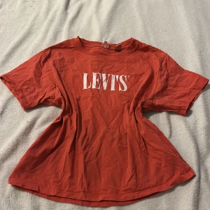 Rosa/orange t-shirt från Levi's - Säljer en rosa/orange t-shirt från Levi's med vit logga på bröstet. T-shirten har en klassisk rund hals och korta ärmar. Perfekt för en avslappnad stil.