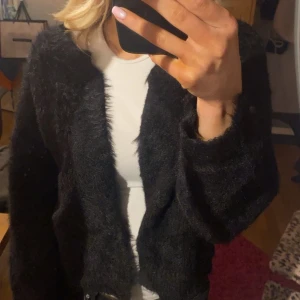 Svart fluffig kofta - Säljer en mysig svart fluffig kofta med långärmad design. Koftan har en enkel och elegant look som passar till många olika outfits.