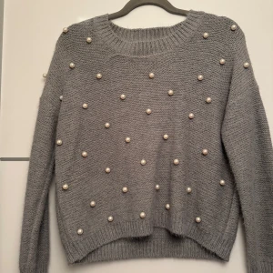 Grå stickad tröja med pärlor - Säljer en mysig grå stickad tröja dekorerad med pärlor. Tröjan har långa ärmar och en rund halsringning. Perfekt för att ge en stilren touch till din outfit. Passar bra till både jeans och kjol.