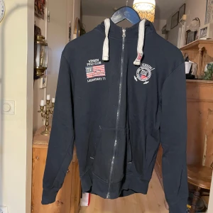 Marinblå zip up hoodie från Vinson Polo Club - Säljer en marinblå zip up hoodie från Vinson Polo Club med dragkedja och tryck på bröstet. Den har en justerbar huva med snören och långa ärmar. Perfekt för en avslappnad stil. 🖤
