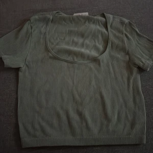 Grön ribbad topp - Säljer en stilren grön ribbad topp med korta ärmar och rund halsringning. Perfekt för en avslappnad look. Passar bra till jeans eller kjol.
