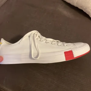 Vita sneakers från Converse - Snygga vita Converse sneakers med röd detalj på tån och leopardmönstrad innersula (kan byta). Skorna har klassisk snörning och en svart sula. Perfekta för en stilren look och till våren som närmar sig! Helt oanvända och till mycket bra pris<3 hör av er vid minsta intresse😊
