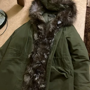 Grön parkajacka från Hollies - Säljer en snygg grön parkajacka från Hollies med en fluffig pälsdetalj runt huvan. Jackan har en quiltad insida och praktiska fickor framtill. Perfekt för kyliga dagar