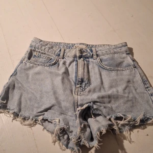 Ljusa jeansshorts från Gina Tricot - Snygga ljusa jeansshorts från Gina Tricot med fransiga kanter för en avslappnad look. Perfekta för sommardagar och festivaler. De har en klassisk femficksdesign och är tillverkade i ett slitstarkt denimtyg.