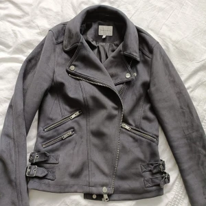 Grå mockajacka från Bershka - Snygg grå mockajacka från warehouse med dragkedjor och bältesdetaljer. Jackan har en klassisk bikerstil med asymmetrisk dragkedja och flera fickor. 