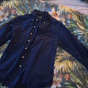 Mörkblå skjorta från Ralph Lauren - Snygg mörkblå skjorta från Ralph Lauren i slim fit. Skjortan har långa ärmar och knappar framtill. Perfekt för en stilren look med den ikoniska loggan broderad på bröstet.