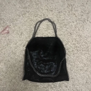 Svart väska med kedjedetaljer - Snygg svart väska med kedjedetaljer och leopardmönstrat foder. Perfekt för att ge din outfit en edgy touch. Väskan har en rymlig insida med plats för det mesta du behöver ha med dig.