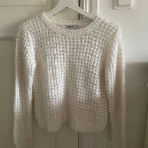 Vit stickad tröja från Gina Tricot - Mysig vit stickad tröja från Gina Tricot i storlek S. Tröjan har en fluffig textur och långa ärmar, perfekt för kyligare dagar. Den har en rund halsringning och ribbade muddar vid ärmslut och nederkant.