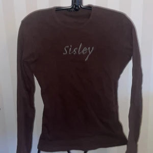 Brun långärmad tröja från Sisley st.146-152 - Säljer en brun långärmad tröja från Sisley med märkesnamnet broderat på framsidan, etikett bortklippt så uppskattningsvis st.146-152 . Mått över ryggen 40 cm, armlängd 56 cm.Perfekt för en stilren och enkel look. Tröjan har en normal passform och är tillverkad i ett mjukt material.