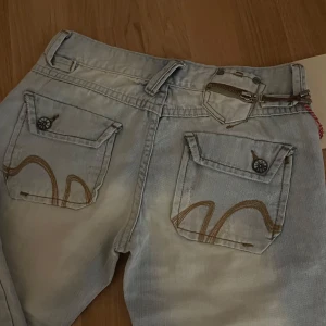 Ljusblå jeans med broderade detaljer - Snygga ljusblå jeans med unika broderade detaljer på bakfickorna. De har en klassisk femficksdesign och en dragkedja med knappstängning. Perfekta för dig som vill ha något lite extra i garderoben!