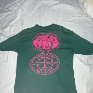 Grön t-shirt med tryck - Säljer en grön t-shirt med ett stort rosa tryck på baksidan och ett mindre på framsidan.  Kostar runt 300kr på junkyard märket är junkyard egna 