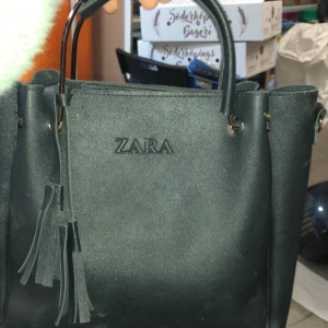 Svart handväska från Zara - Snygg svart handväska från Zara med stilrena fransdetaljer. Väskan har två handtag och en enkel design som passar perfekt för alla tillfällen. Tillverkad i syntetmaterial för en modern look.