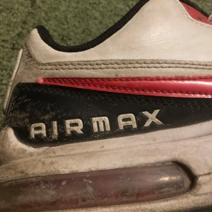 Nike Air Max sneakers i vitt och rött - Säljer ett par klassiska Nike Air Max sneakers i vitt med röda och svarta detaljer. Skorna har den ikoniska Air Max-dämpningen och snörning framtill. Perfekta för en sportig look.