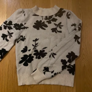 Beige tröja med blommönster från VILA - Säljer en beige tröja från VILA med ett svart blommönster. Tröjan har långa ärmar och en rund halsringning.