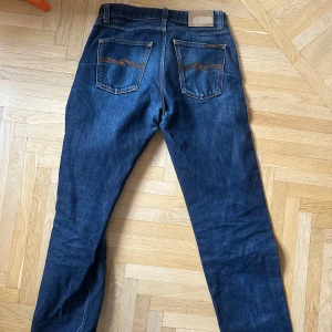 Rad Rufus Nudie - Snygga mörkblå jeansbyxor med klassisk femficksdesign och dragkedja. De har en straight passform och är perfekta för en avslappnad stil. Byxorna har en midwaist och är tillverkade i slitstarkt denim.