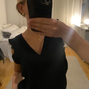 Gullig svart topp med volanger i ärmarna - Säljer en stilren svart ärmlös topp från H&M i storlek XS. Toppen har en v-ringad design och volangdetaljer vid ärmarna. Perfekt för en elegant och enkel look. Jättesöt och nästan aldrig använd. Jag är en person som brukar ha strl XS. Hör av dig om du undrar något eller diskutera priset!❤️
