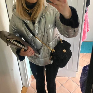 Silverfärgad pufferjacka - Snygg och glansig silverfärgad pufferjacka med dragkedja och luva. Perfekt för kyliga dagar med sin quiltade design. Jackan har långa ärmar och en modern look.