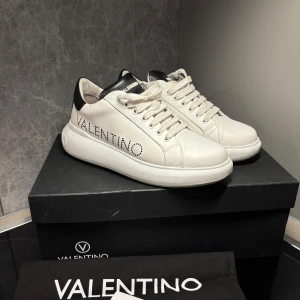 Vita sneakers från Valentino - Snygga vita sneakers från Valentino med svart detalj på hälen och märkeslogga på sidan. Skorna har snörning och en stilren design som passar perfekt för en trendig look.