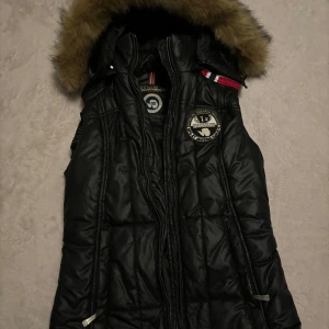 Svart dunjacka från Napapijri - Snygg svart dunjacka från Napapijri med avtagbar huva och pälsdetaljer. Jackan har en broderad logotyp på bröstet och dragkedja framtill. Perfekt för kyliga dagar med sin vindtäta och vattentäta design. Obs dragkedjan är trasig 