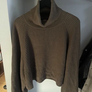 Brun stickad polotröja från Bik Bok - Säljer en väldigt mörk grön stickad polotröja från Bik Bok. Tröjan har en hög krage och långa ärmar den är även mer åt de croppade hållet i midjan. 