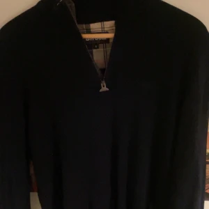 Svart tröja med dragkedja från Barbour - Säljer en stilren svart tröja från Barbour med dragkedja i halsen. Perfekt för kyligare dagar och ger en klassisk look. Tröjan har en diskret design som passar till många tillfällen.