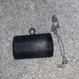Svart glittrig kuvertväska med kedja - Snygg svart kuvertväska med glittrig yta och en elegant kedja för axelrem. Perfekt för en kväll ute eller speciella tillfällen. 