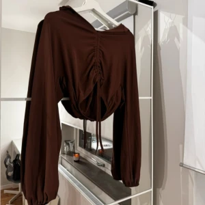 Brun långärmad tröja med snörning - Snygg brun tröja med långa ärmar och trendig snörning framtill. Perfekt för en stilren look med en twist. Passar bra till både jeans och kjol.