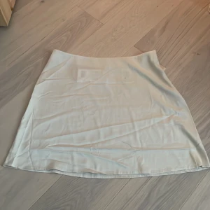Beige kjol från Monki - Snygg beige/vit kjol från Monki i en stilren design. Kjolen har en dragkedja på sidan för enkel på- och avtagning. Perfekt för en minimalistisk look. Mer som en 40 i storlek. Helt oanvänd nypris 250kr