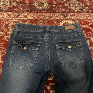 Blå bootcut jeans från Bongo - Snygga blå bootcut jeans från Bongo med klassisk femficksdesign och dekorativa sömmar på bakfickorna. Perfekta för en avslappnad stil. Dem sitter lågmidjat och dem passar mig som är 170 och dem är tom lite längre än till mina hälar för oss tall girls🫶🏼