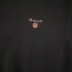 Svart tröja från GANT - Säljer en stilren svart tröja från GANT i premium bomull. Tröjan har en diskret logga på bröstet och rund halsringning med ribbade kanter. Perfekt för en klassisk look.