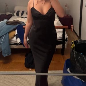 Svart sidenklänning med smala axelband - Elegant svart klänning i siden med smala axelband och v-ringad design. Perfekt för en stilren och sofistikerad look. Klänningen har en figurnära passform och når till knäna. Helt ny med prislapp. Köpt för 500kr 