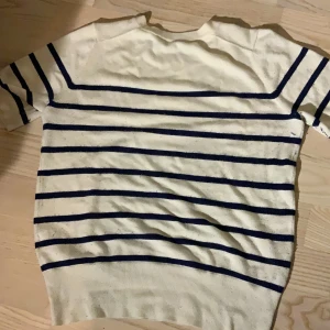 Vit och marinblå randig tröja från Zara - Säljer en stilren vit tröja med marinblå ränder från Zara. Tröjan har korta ärmar och en klassisk rund halsringning. Är lite nopprig från användning 
