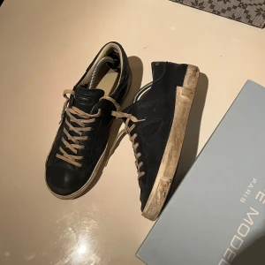 Philippe Models - Snygga svarta sneakers från Philippe Model med vita sulor och beige snörning. Perfekta för en stilren look. Skorna har en klassisk design med en diskret logga på sidan. Sparsamt använda. Obs ej og box! Priset är diskuterbart