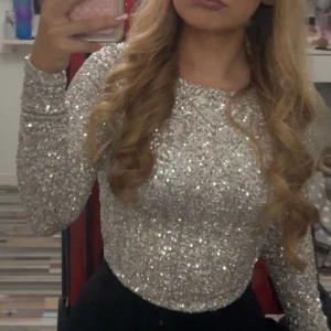 Glittrig silvertröja - Säljer en glittrig silvertröja med långa ärmar. Perfekt för festliga tillfällen med sitt paljettmönster som ger en extra touch av glamour. Tröjan har en tight passform och är croppad för en modern look. Samt backless . klippte tyvärr av taggen för den kliade och stack ut men den är köpt på newyorker för 200kr.  Använde den själv en gång. priset går att diskutera 😊