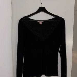 Svart långärmad topp från Hunkemöller - Snygg svart långärmad topp från Hunkemöller med v-ringad spetsdetalj. Perfekt för en stilren look. Tillverkad i ett mjukt material som ger en bekväm passform.