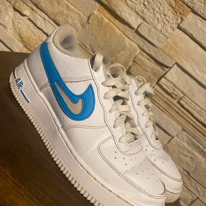 Nike Air Force 1 -   Nike Air Force 1 Low GS White Aqua – Storlek 38,5 EU  Säljes ett par Nike Air Force 1 Low GS i färgen White Aqua. Skorna har en stilren vit överdel i läder med den ikoniska Swoosh-loggan i blått (Aqua). 	•	Storlek: 38,5 EU 	•	Modell: Nike Air Force 1 Low GS White Aqua 	•	Skick: Skorna har tecken på användning, men är fortfarande i bra skick för att användas. De kan behöva en lätt rengöring för att återfå sin fulla potential.  Perfekta för dig som letar efter et