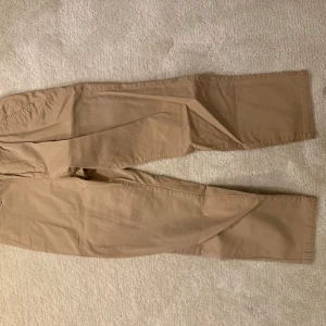 Beige chinos - Snygga beige chinos med normal passform. Byxorna har knappar och dragkedja i gylfen samt bälteshällor. Perfekta för en stilren look. Storlek 32/32. Mycket bra skick.