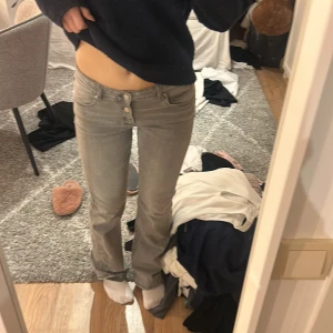 Grå jeans med låg midja - Snygga grå jeans med låg midja och bootcut-stil. De har en klassisk femficksdesign och knappar framtill. Perfekta för en avslappnad look.