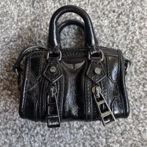 Mini väska zadig - Snygg svart handväska i skinn med stilrena metallspännen och dubbla handtag från zadig voltaire. Perfekt för att ge en edgy touch till din outfit. Väskan har en kompakt design som gör den lätt att bära med sig.