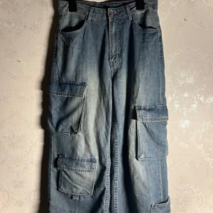 Blå cargo jeans  - Midja: 35cm. längd (utsida av byxan): 89cm. innerlängd: 57,5cm. bredd längst ner på benen: 29cm. OBS de är uppsydda och passar någon som är runt 150-155cm lång