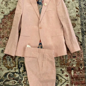 Ljusrosa kostym  - Snygg ljusrosa kostym från Isaac Dewhirst med en kavaj och matchande byxor. Kavajen har en blommig insida i färgglada nyanser och en enkel knapp framtill. Perfekt för sommarens festligheter!