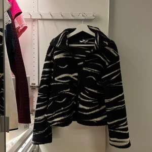 Teddyjacka Zebra - Säljer en svart och vit teddyjacka med zebramönster. Jackan har en mjuk och fluffig textur, perfekt för att hålla sig varm under hösten/våren. Den har långa ärmar och en bekväm passform. Så så så snygg!! Knappast använd! Skriv vid frågor! 