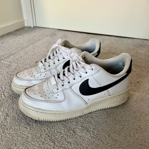 Nike Air Force 1’07 - Nike Air Force sneakers i vitt med svarta detaljer. De är använda men fortfarande i relativt bra skick!! Se bilder för små defekter. Köptes för ca 1200kr. 