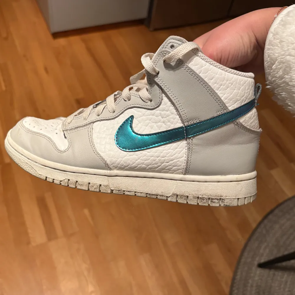 Snygga vita Nike sneakers med en metallicblå swoosh och snörning. Skorna har en hög modell. Kengät.