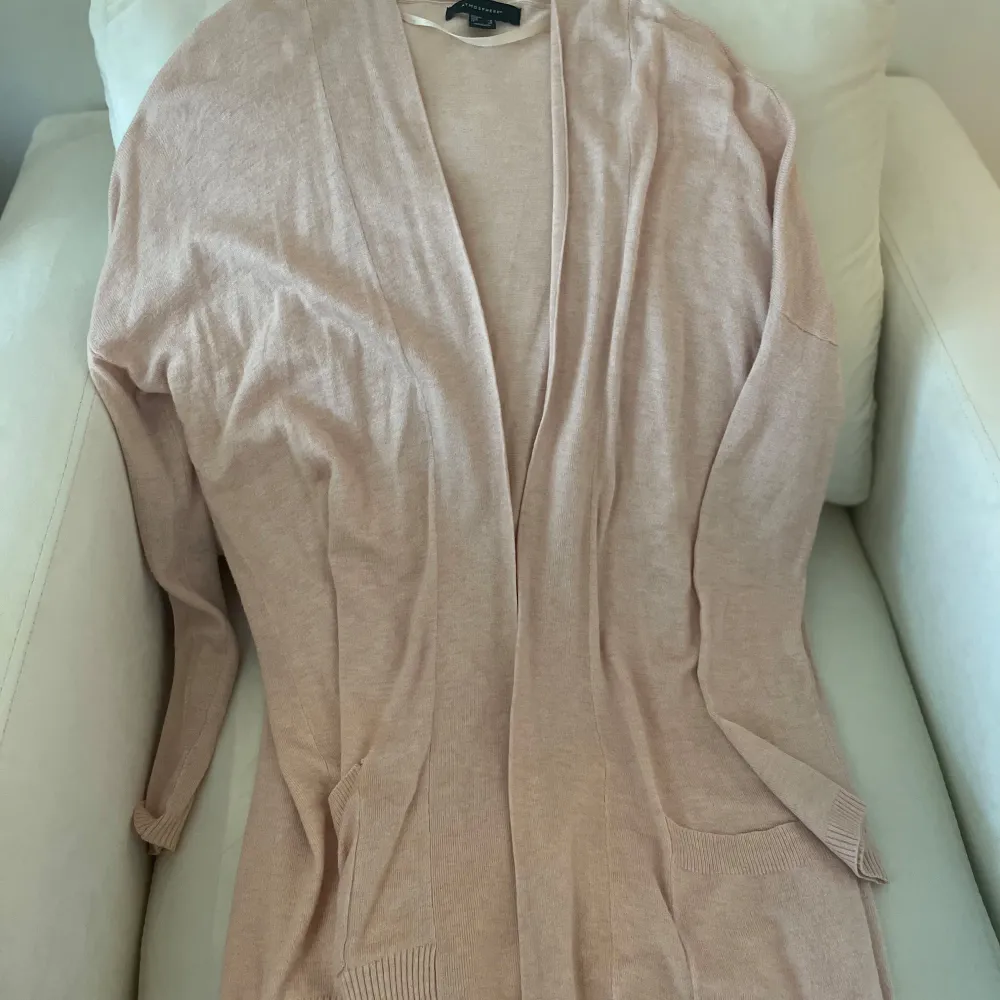 Mysig beige kofta från Atmosphere i ett mjukt material. Perfekt för lager-på-lager under höst och vår. Den har långa ärmar och en öppen design utan knappar, vilket gör den lätt att matcha med olika outfits. Perfekt för en avslappnad och stilren look!. Neuletakit & Villapaidat.