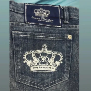 Jeansshorts med broderad krona - Snygga jeansshorts från Victoria Beckham med en cool broderad krona på bakfickan. De är i en mörkblå denim med fransiga kanter för en avslappnad look. Perfekta för sommardagar eller festivaler!
