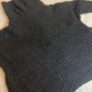 Mörkgrå ribbad polotröja med öppen rygg - Säljer en stilren mörkgrå ribbad polotröja med hög krage, med en öppen rygg. Perfekt för kyliga dagar och ger en mysig känsla. Tröjan har långa ärmar och är tillverkad i ett mjukt material.❤️