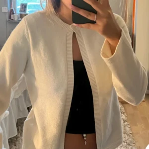 Vit kofta inte min bild  - Säljer en stilren vit kofta i mjukt material. Perfekt för både vardag och fest. Den har långa ärmar och en enkel design utan knappar, vilket gör den lätt att matcha med olika outfits. Passar bra till både jeans och klänning.